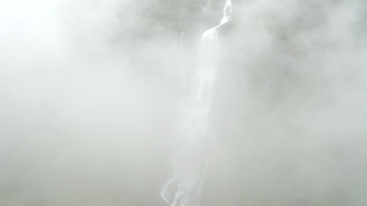 Shoot of Waterfall in Norway. Drone increasing altitude rising in clouds. Majestic dreamy look.