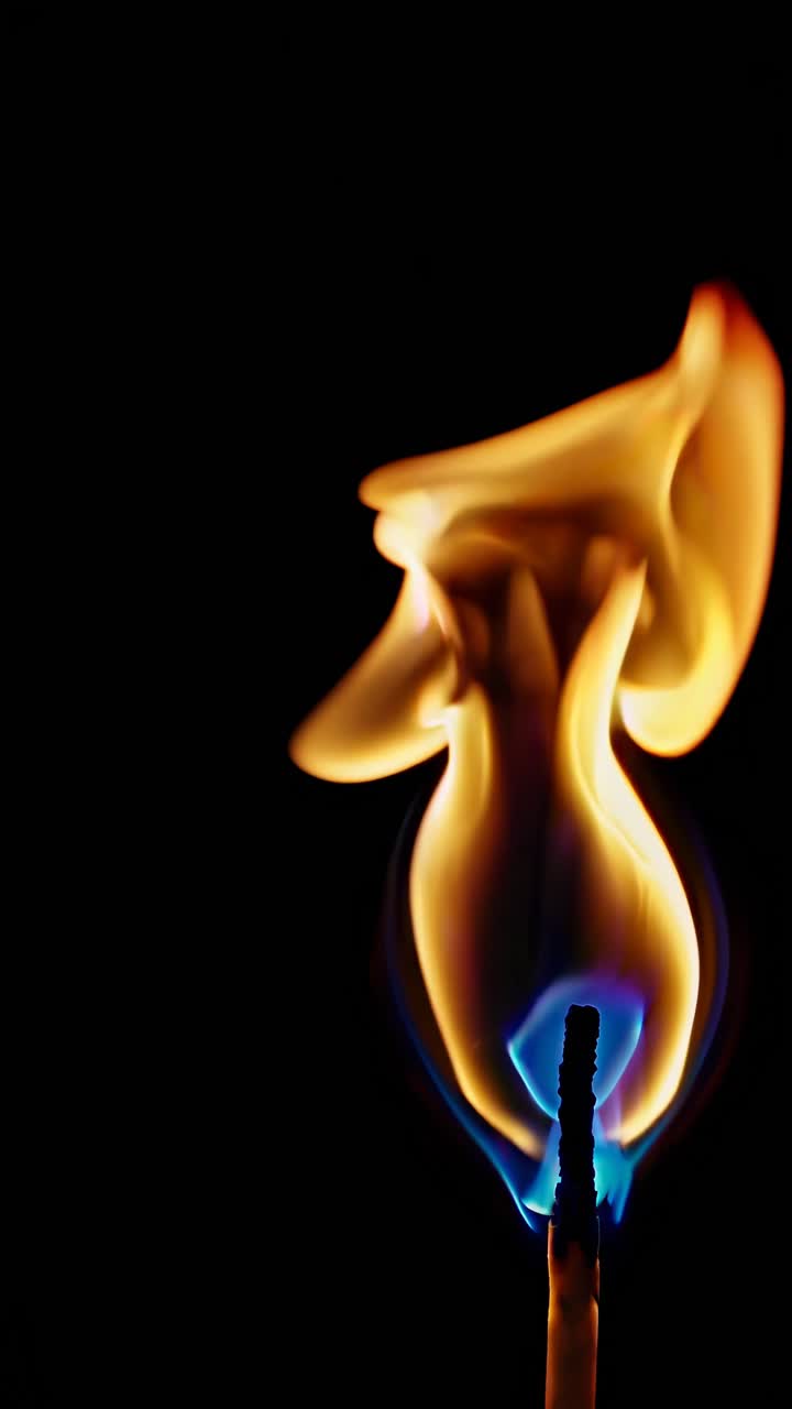 Close-up, low-angle shot of a matchstick flame against a dark background, capturing the flickering