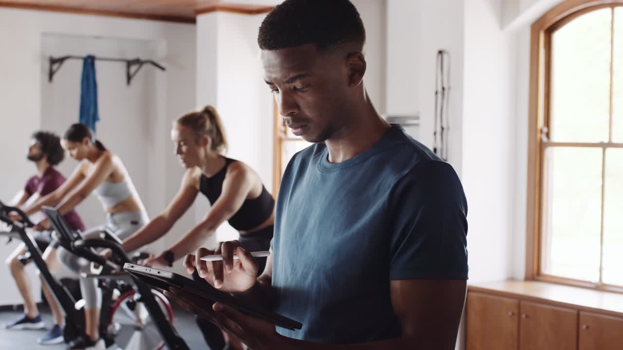 자신감 있고 지식이 많은 젊은 성인 흑인 남성이 실내 체육관에서 태블릿을 사용하고 있습니다.
