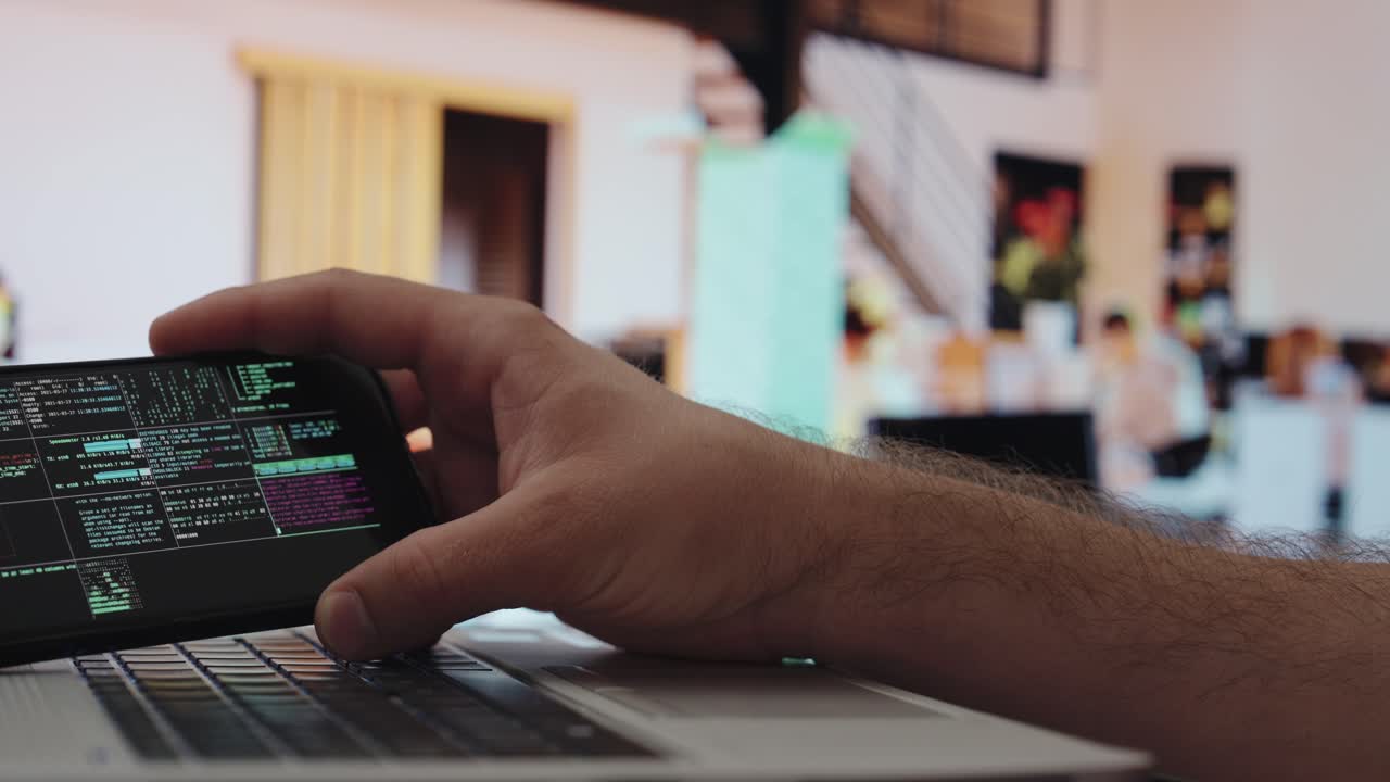 A hand holds a phone with AI code over a laptop in a bright office — symbolizing how artificial intelligence becomes part of modern digital work life