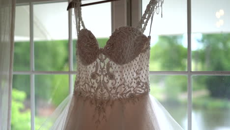 bride's wedding dress hanging from window beautiful detailed corset top with full skirt