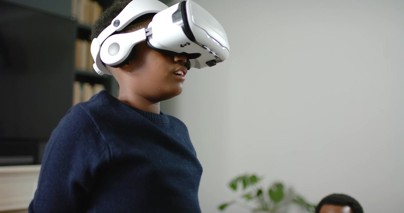 Afroamerikansk mand og ung person sidder på sofaen med en tablet, mens den unge tager et VR-headset på og udforsker.