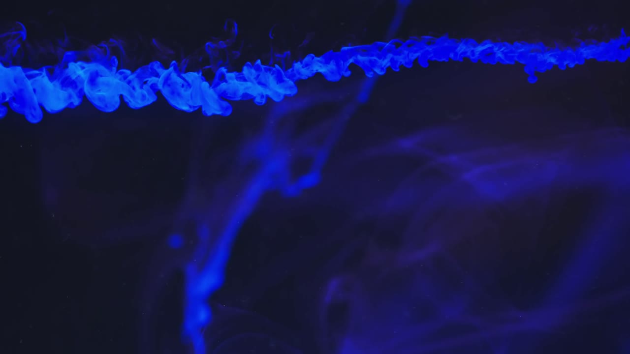 video en cámara lenta de tinta de acuarela azul mezclándose en agua contra un fondo negro