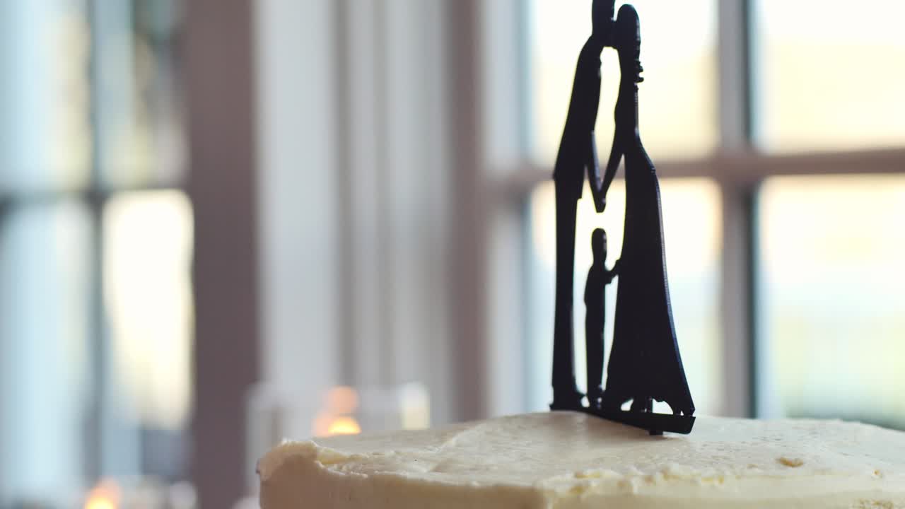 Cake topper nuziale con famiglia di tre persone, con finestra e candele sullo sfondo.