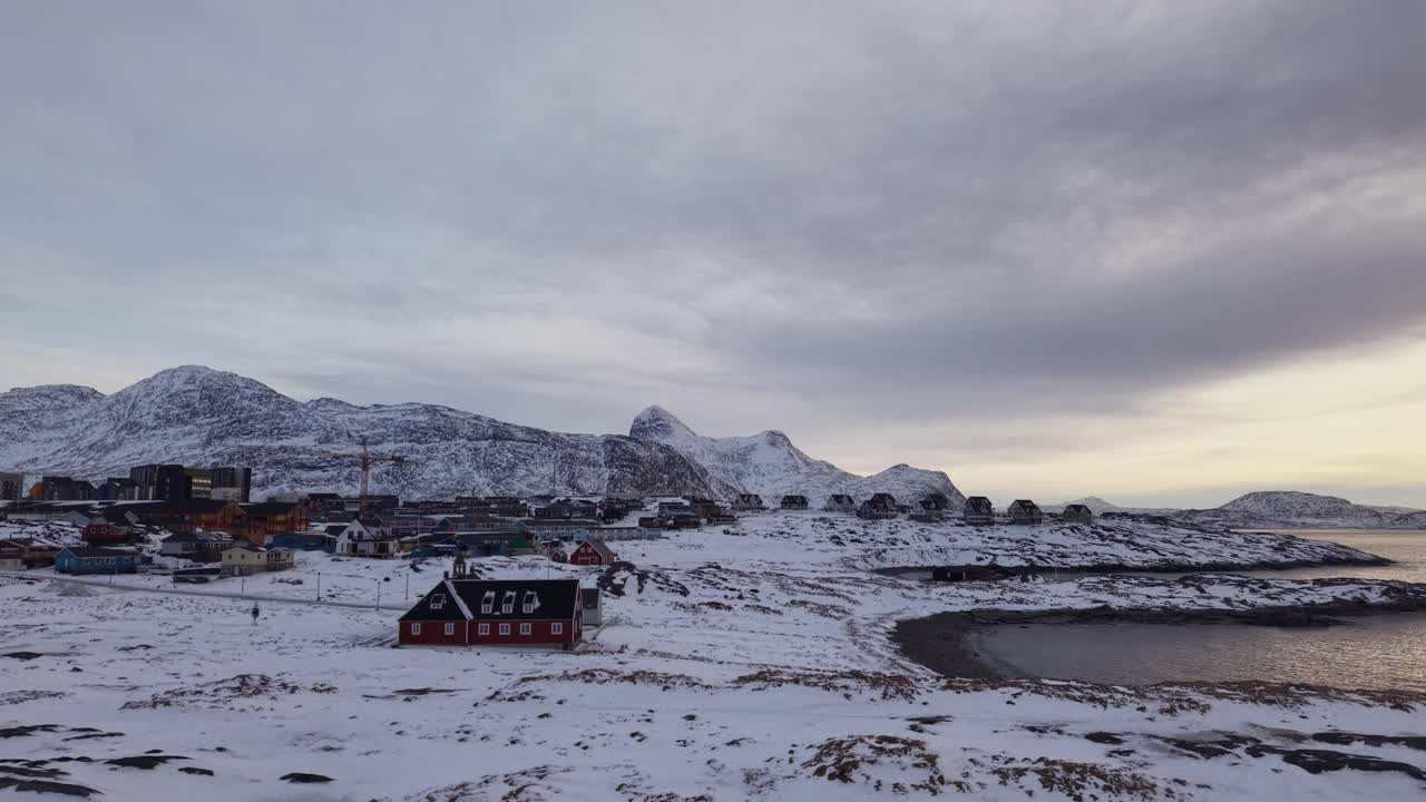 凍てつく北極の海岸線に沈む、息をのむほど美しい黄金の夕日。雪に覆われた岩々と、ドラマチックな冬空の下で太陽の光を反射する穏やかな氷の海が特徴です。