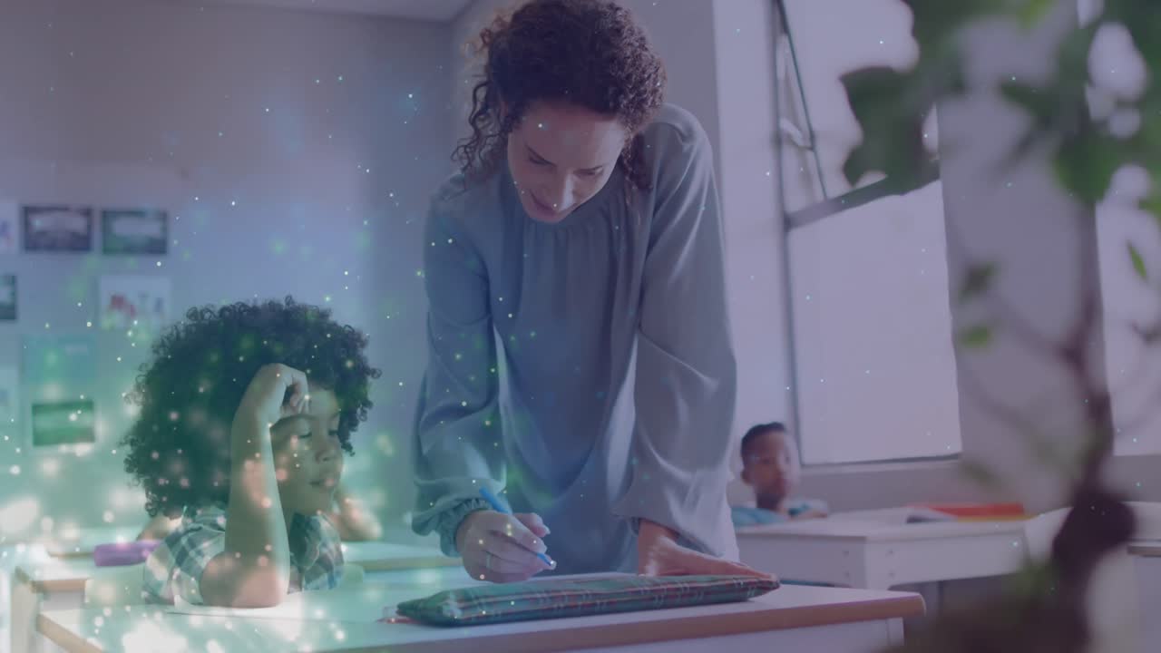 Animation of light particles over happy diverse female teacher helping schoolboy at desk in class