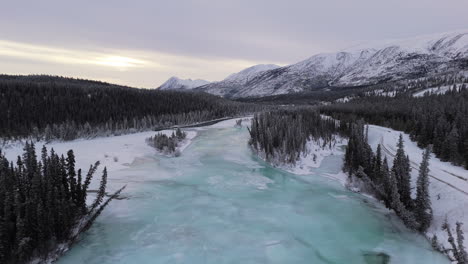 a smooth aerial dolly forward shot travels over icy trees and the frozen takhini river with a majestic mountain backdrop. this dynamic footage captures the pristine winter landscape of yukon