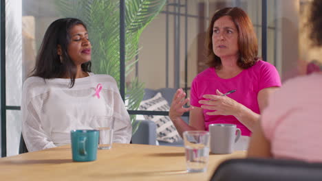 counsellor at meeting of therapy support group for cancer treatment patients talking with women wearing pink breast cancer awareness ribbons