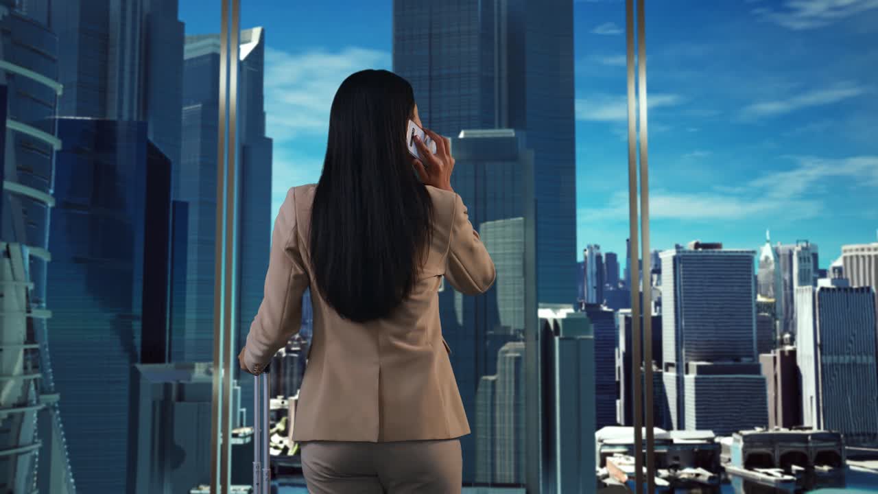 가방을 들고 걸어다니는 아시아 사업가 여성이 스마트폰으로 대화를 나누고 창밖에서 초고층 건물이 있는 큰 도시를 바라보고 있습니다.
