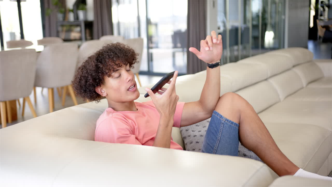 Talking on smartphone, young man relaxing on couch in modern living room