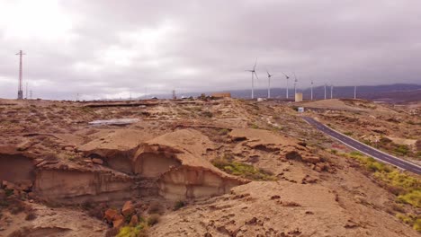 Rocky-desert-landscape-with-road-and-windmills-in-distance,-aerial-view