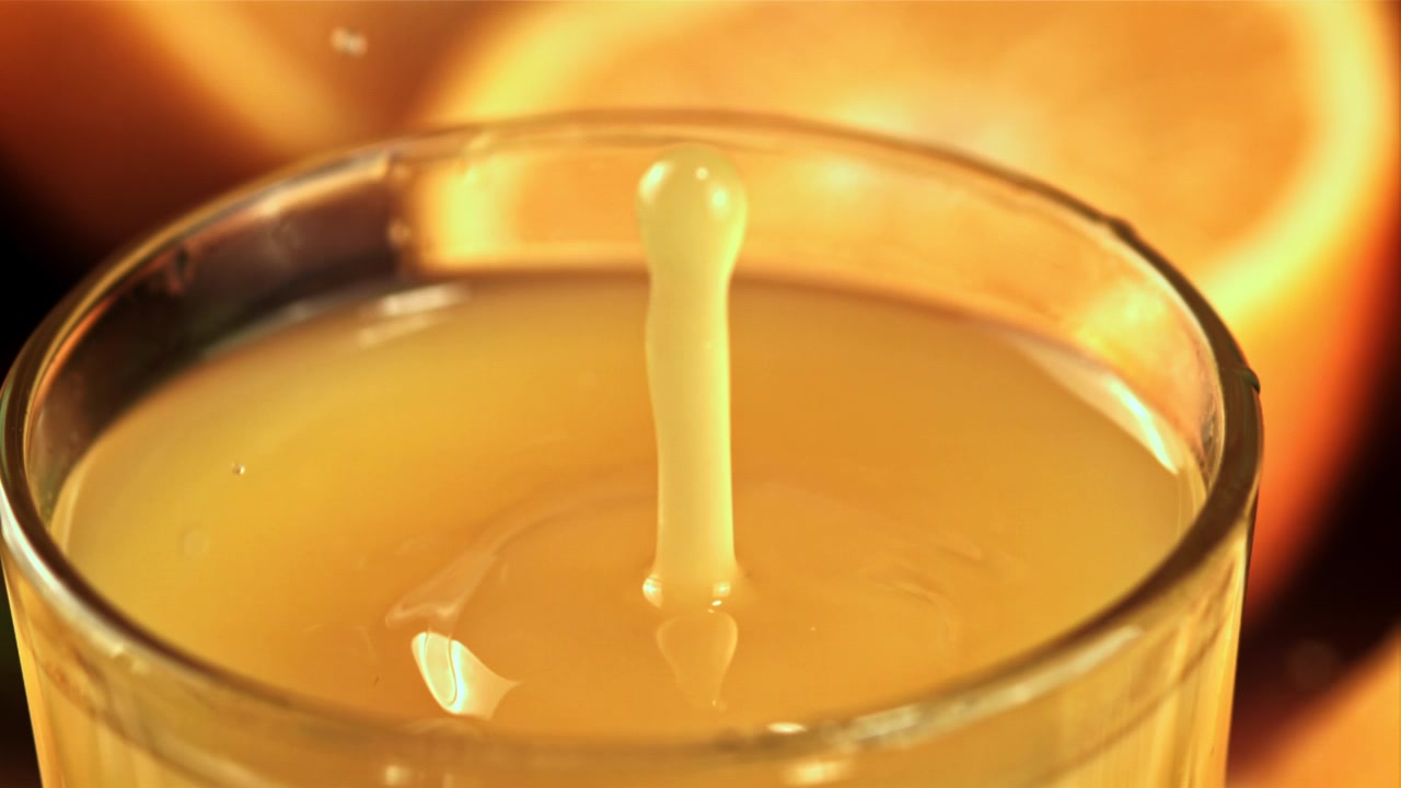 Goccia al rallentatore che schizza in un bicchiere di succo d'arancia fresco