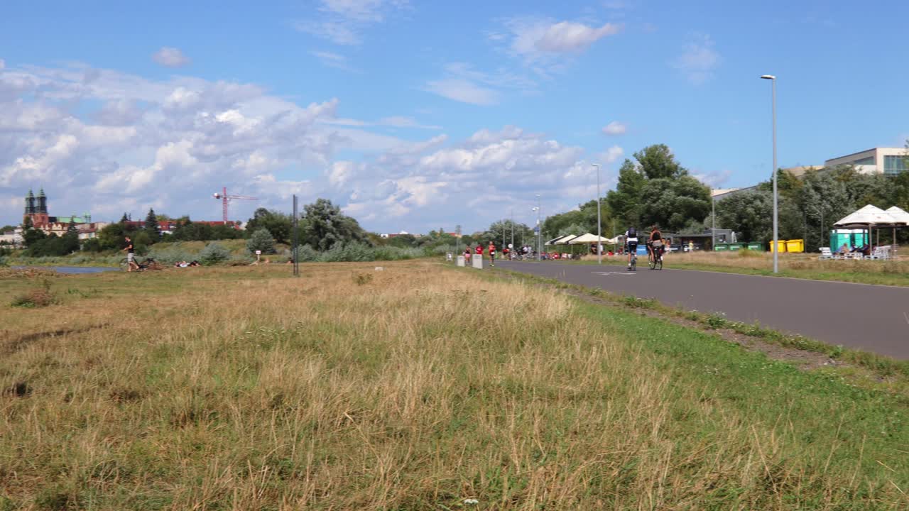Panning shot of people cycling along Warta river in Poznan during sunny weather in Poznan.