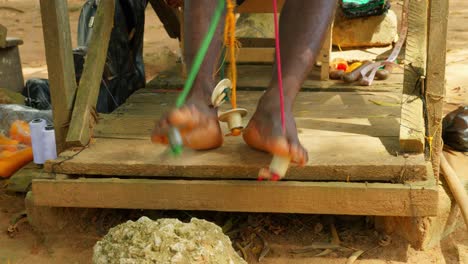 los pies de un hombre africano tejiendo tela en un telar de madera