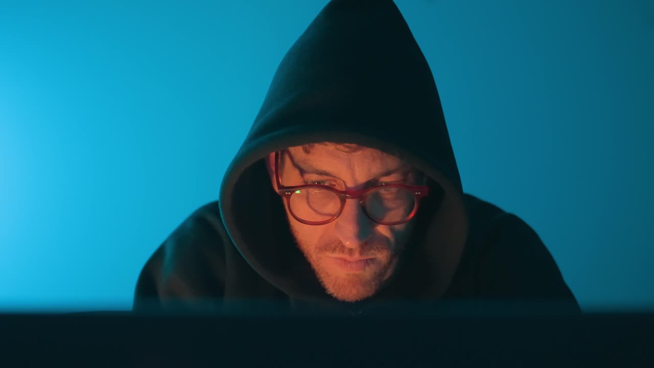 Hacker con felpa con cappuccio seduto dietro un laptop con luce blu e arancione drammatica, cybersicurezza, hacking, frode online, privacy dei dati, computer segreto. frode online, privacy dei dati, vista frontale. uomo computer