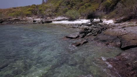 Antena:-Una-Toma-Hacia-Atrás-A-Baja-Altura-Que-Revela-Una-Costa-Rocosa,-Rocas-Y-Una-Isla-Tropical-Mientras-Aumenta-Lentamente-La-Altitud-Y-Vuela-Constantemente-Hacia-Atrás,-Tailandia