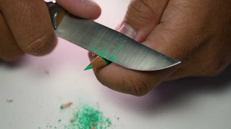 Footage of hands slowly sharpening a pencil and some coloured pencils with a sharp knife