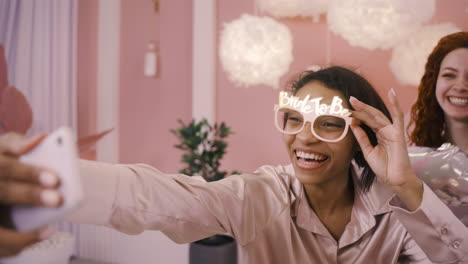 vista de cerca de una mujer con gafas con una frase de novia a novia sosteniendo un teléfono inteligente para tomar una selfie con sus amigas en una despedida de soltera