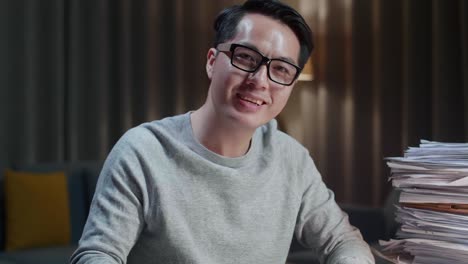 집에서 문서를 처리하는 동안 카메라에 미소 짓고 팔을 는 아시아 남자의 클로즈업