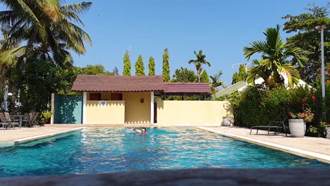 middle aged white man with long hair swimming front crawl and exercising on a hot sunny day in outdoor swimming pool whilst on vacation holiday