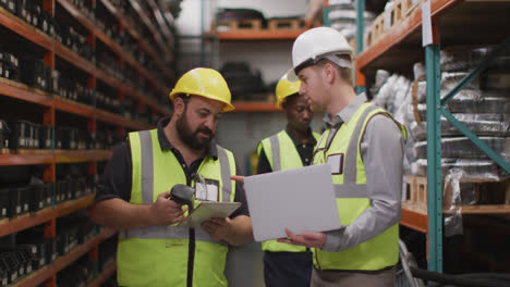 Two-Caucasian-male-factory-workers-at-a-factory,-wearing-vis-vests-and-hard-hats,-standing