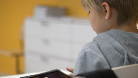 Rear-view-of-young-school-boy-playing-game-on-tablet,-Close-up