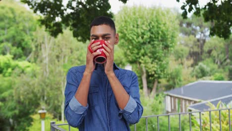 Portrait-of-mixed-race-man-standing-in-garden-drinking-a-mug-of-coffee-and-smiling