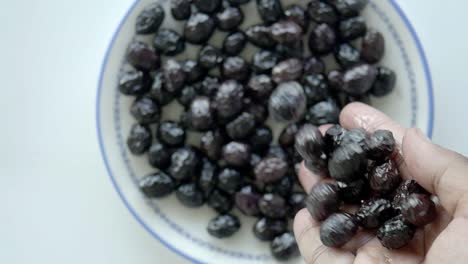 closeup of black olives on a plate with hand holding some olives