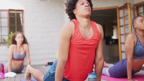 african american man practicing yoga with group of diverse friends in backyard