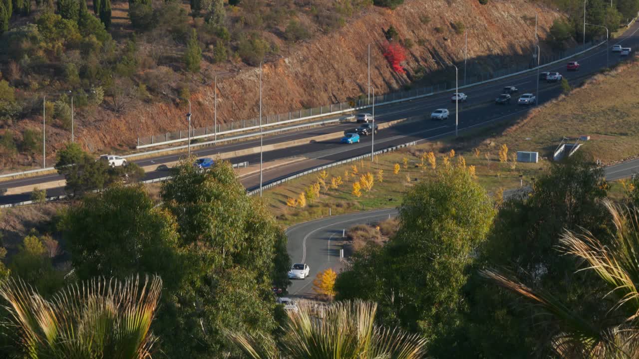 Vehicles move in both directions on a major Canberra highway during late autumn. This slow motion shot captures the orderly rhythm of city life, framed by seasonal hues and soft afternoon sunlight.