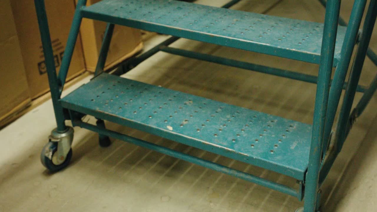 рабочий замыкает нижнюю ступень рулевой лестницы с гофрированным металлом на складе