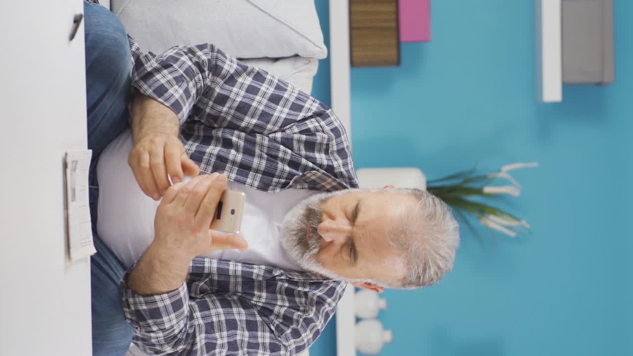 전화로 나쁜 소식을 받은 노인의 수직 비디오입니다.