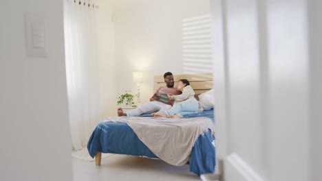 pareja feliz diversa usando la tableta y acostada en el dormitorio
