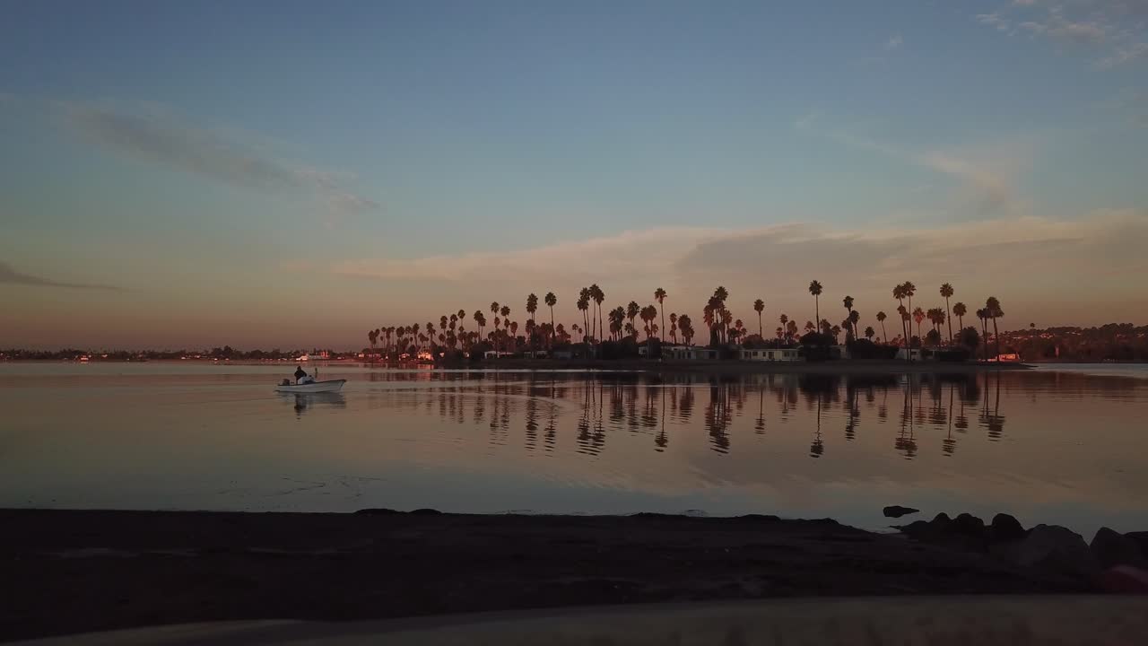 Ripresa statica con drone a Mission Bay alle 6:30 del mattino durante l'alba, con una barca nell'acqua e uccelli che volano attraverso un cielo mattutino sereno.