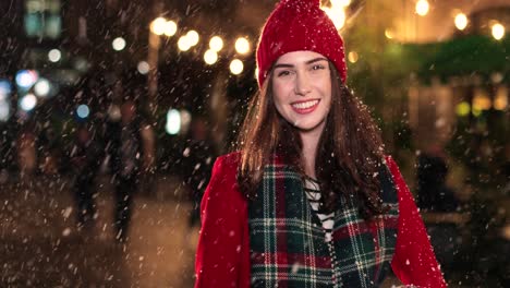 close-up view of caucasian woman in red coat holding a present and smiling at camera on the street while it‚äôs snowing in christmas