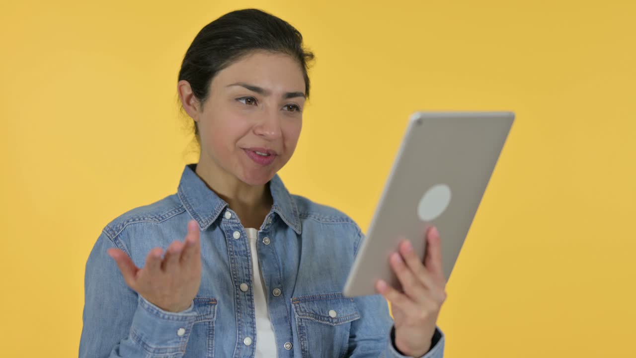 Video Chat on Tablet by Young Indian Woman, Yellow Background