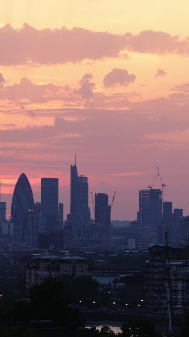 Vista vertical em telefoto do distrito financeiro de Londres com o Gherkin e o 22 Bishopsgate silhuetados sob nuvens de pôr do sol em tons de rosa e laranja ardentes