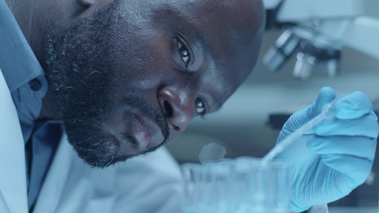 Scienziato afroamericano che aggiunge liquidi chimici in provette con una pipetta