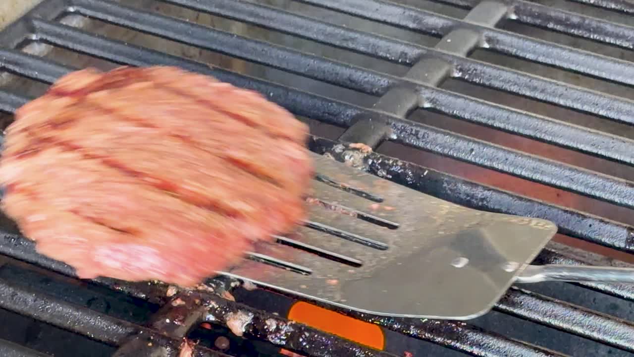 En metallstekespade snur en krydret oksekjøttburger på en varm støpejernsrist