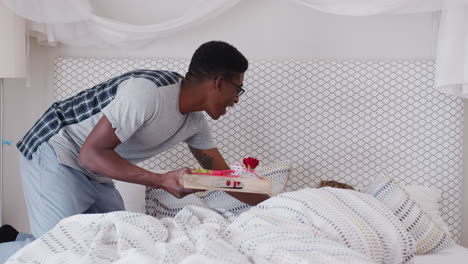 man bringing woman breakfast in bed to celebrate birthday or valentines day