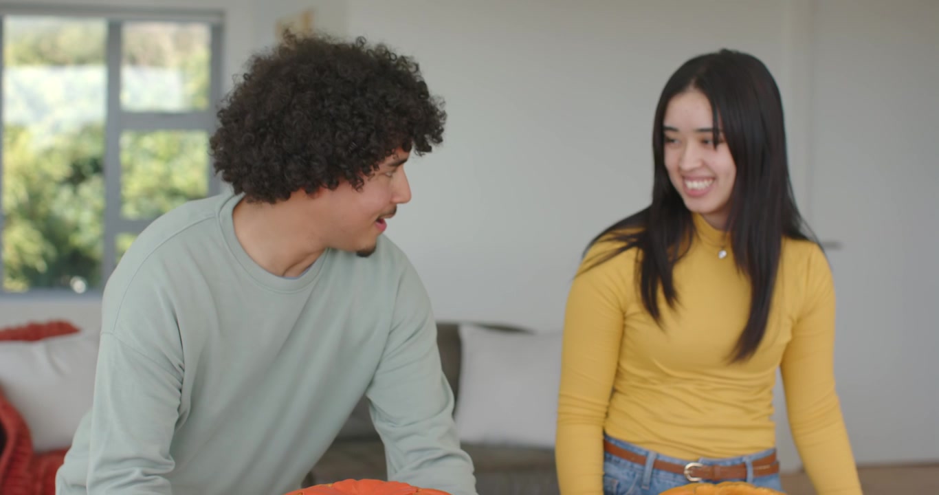 Couple at home smiling as man entering carrying big orange pumpkin, placing pumpkins for halloween