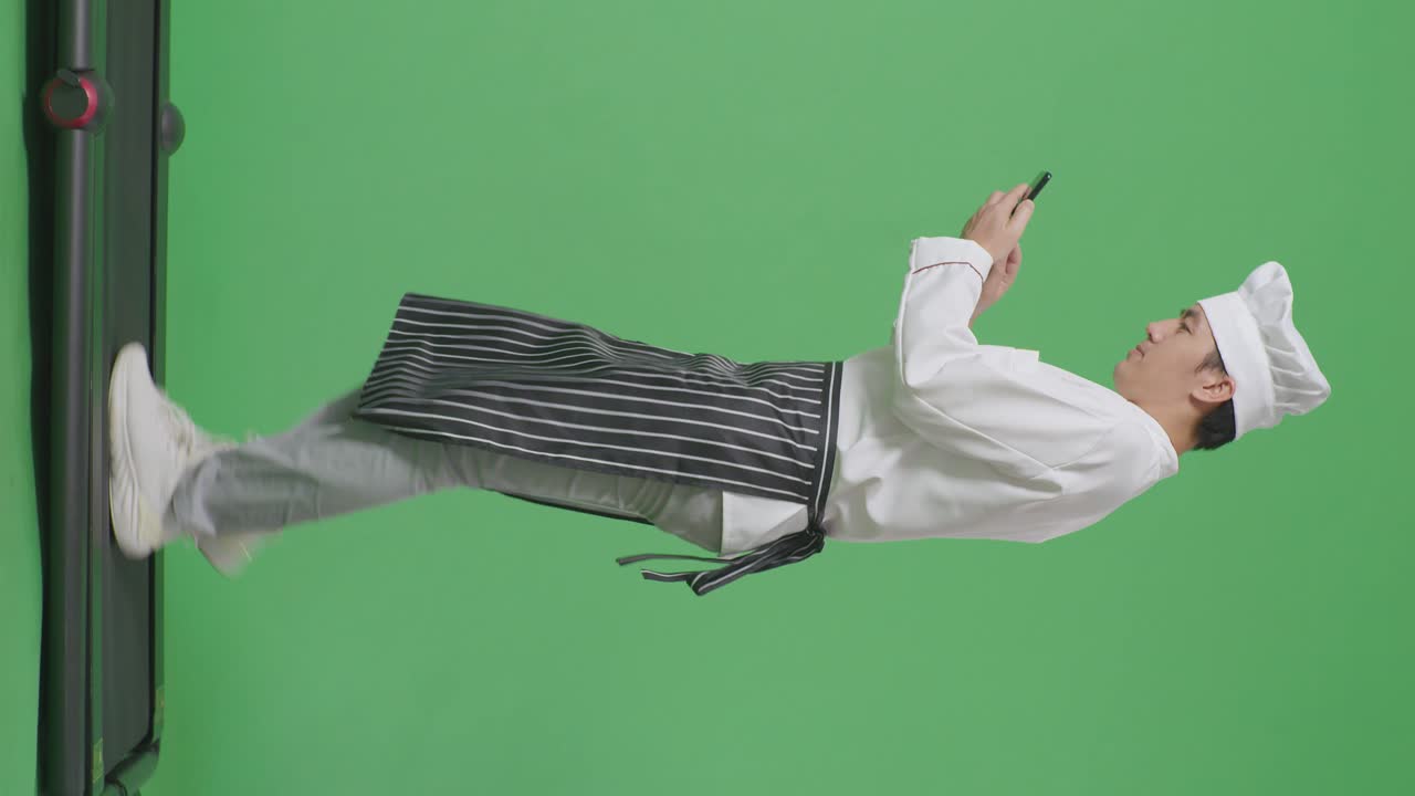 모습으로 가득 찬 몸, 아시아 남성 요리사, 트레드밀에서 고, 녹색 화면 배경 스튜디오에서 스마트폰을 사용한다.