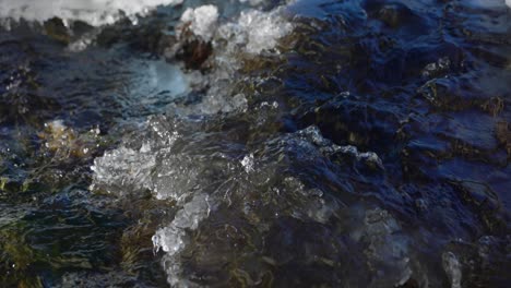 water flows over rocks, snow and ice in shallow stream bed, closeup