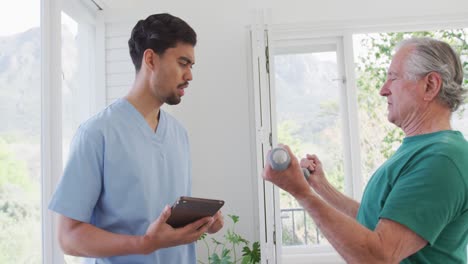 Terapeuta-Masculino-Con-Tablet-Pc-Hablando-Con-Un-Hombre-Mayor-Haciendo-Ejercicio-En-Una-Casa-De-Retiro