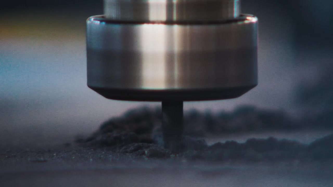 Macro di un mandrino CNC che taglia attraverso polvere e particelle sopra una superficie di legno.