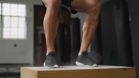 close up of fit caucasian man jumping on pylo box at the gym