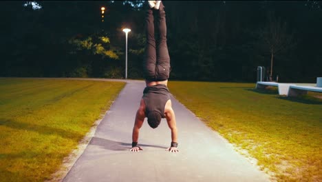 muscular black guy does handstand push up on the middle of the road in a park night time