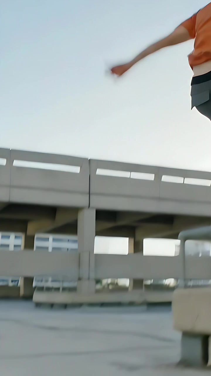 Video verticale: Un adulto con una maglia arancione corre, appoggia il piede e salta sul tetto di un garage, allenandosi.