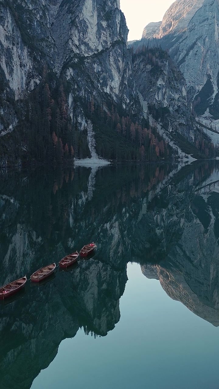 Un sereno lago di montagna riflette le imponenti scogliere e le barche a remi sparse. L'ambiente tranquillo è perfetto per reportage di viaggio o documentari naturalistici.