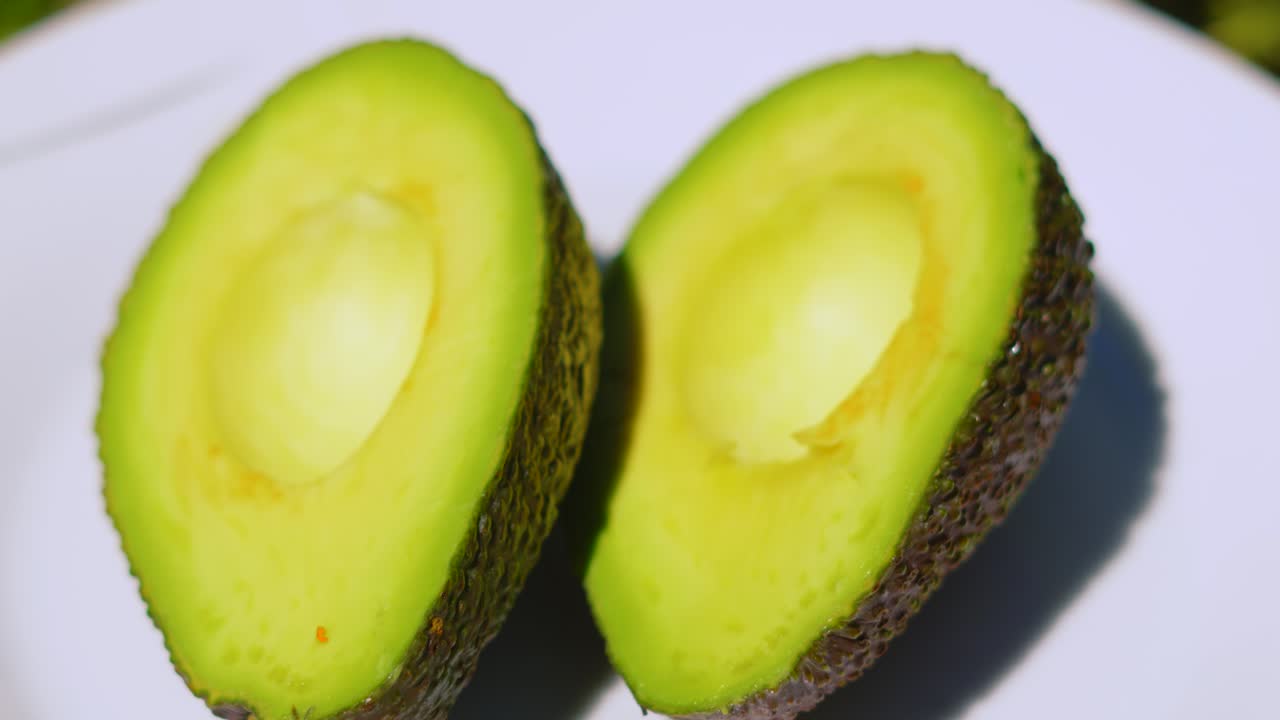 Aguacate fresco cortado por la mitad en un plato blanco bajo la luz natural del sol al aire libre. Alimento saludable y orgánico, fruta y verdura. Consumido en el desayuno o usado en salsas. Rico en grasas insaturadas beneficiosas para el intestino.